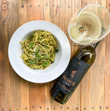 Plate of pasta in pesto sauce next to a bottle of wine and a glass of white wine.