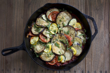 Cast iron dish layered with eggplant, bell peppers, squash, and fresh basil.