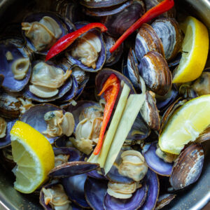 Clams with peppers, lemongrass, and lemon wedges.