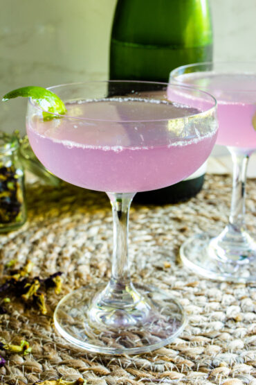 Purple cocktail in a coupe glass with a lime garnish.