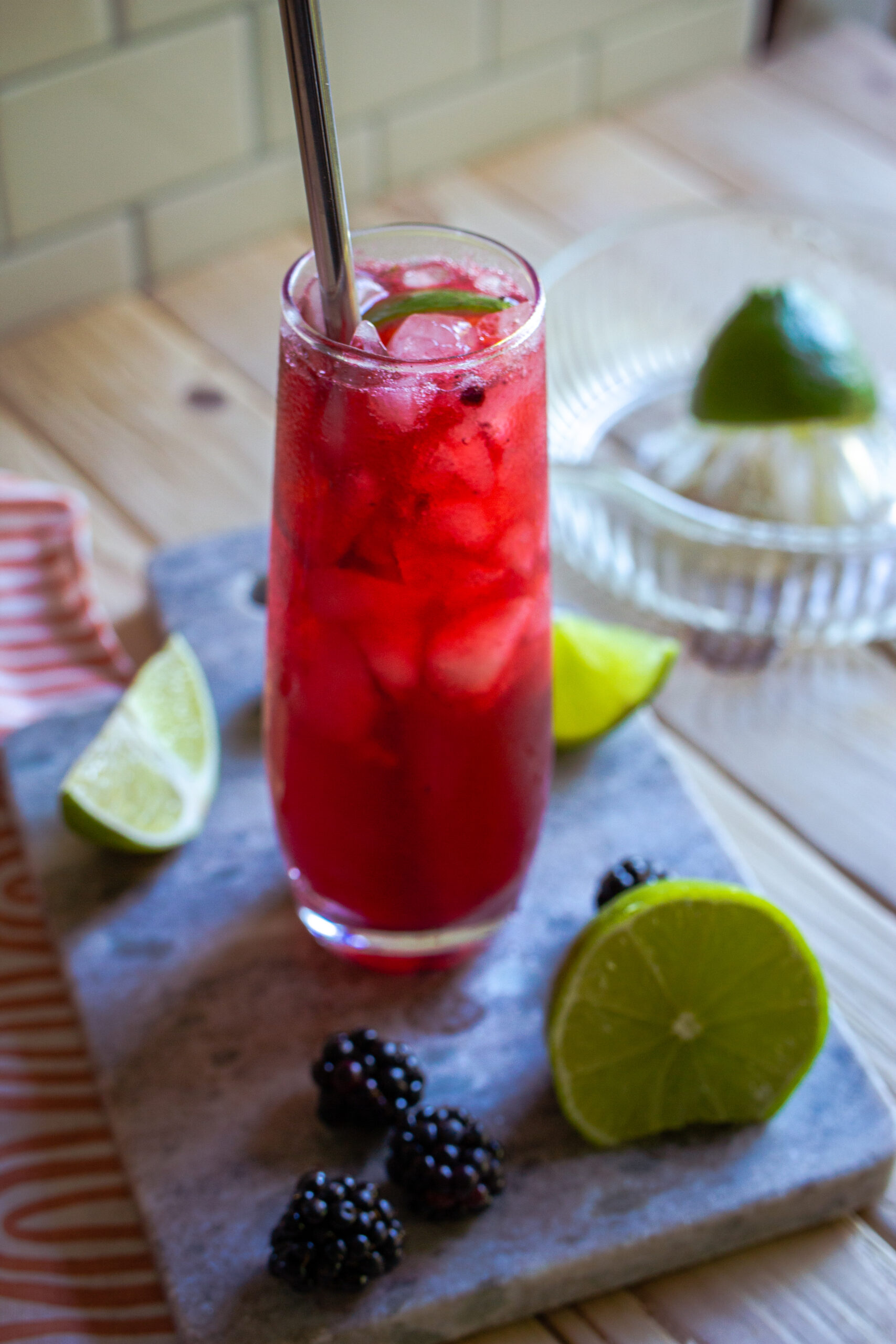 Cocktail in a tall glass with lime wedges and blackberries next to the glass.