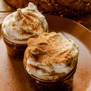 Two ramekins filled with dark chocolate mousse and whipped cream, both dusted with cocoa.