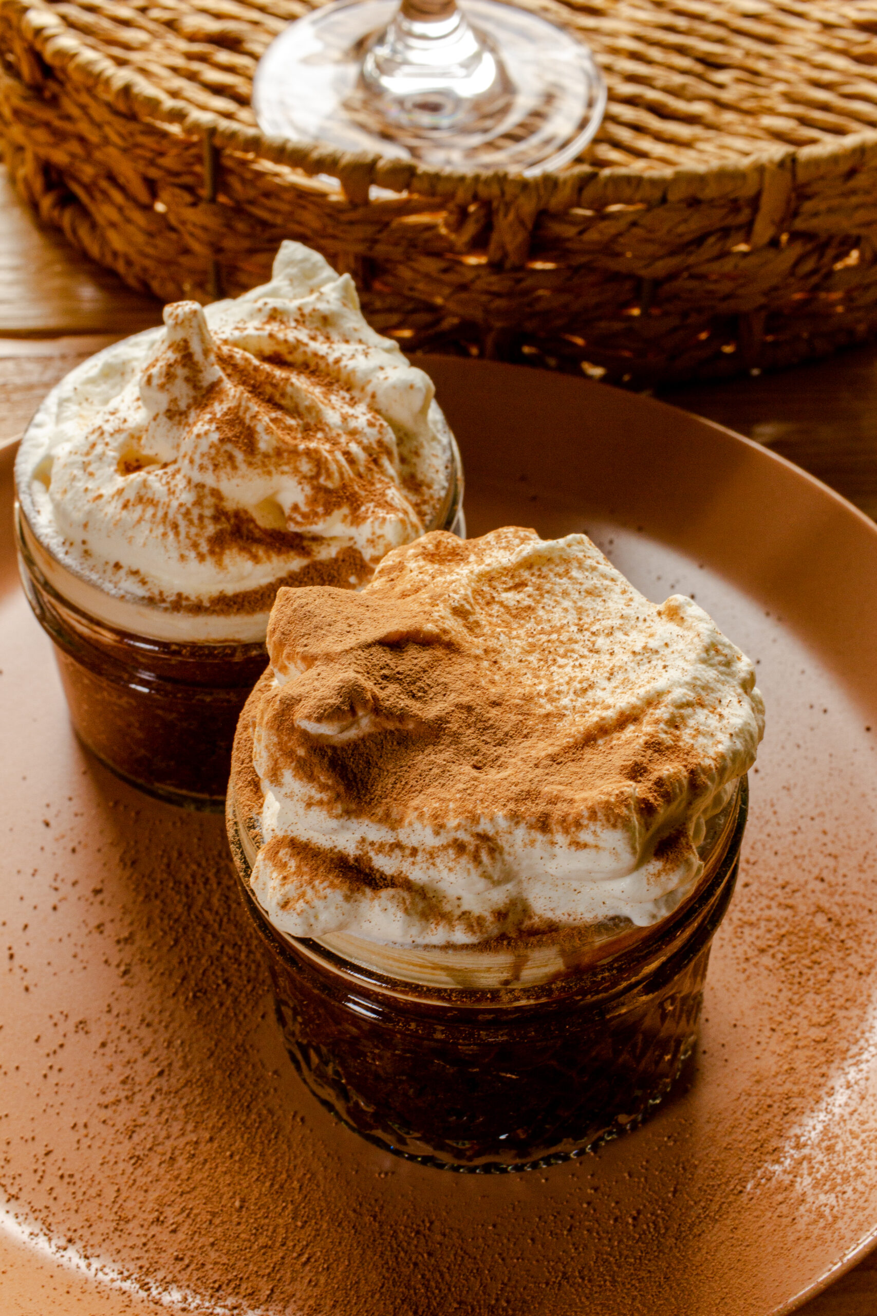 Two ramekins filled with dark chocolate mousse and whipped cream, both dusted with cocoa.