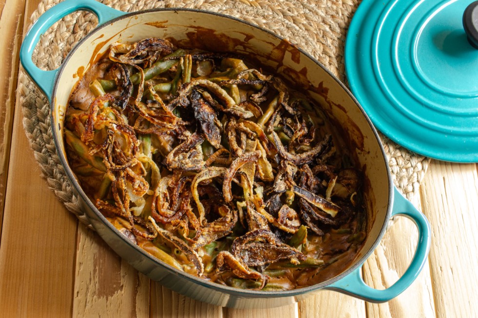 Blue Dutch oven with green bean casserole on wood counter.