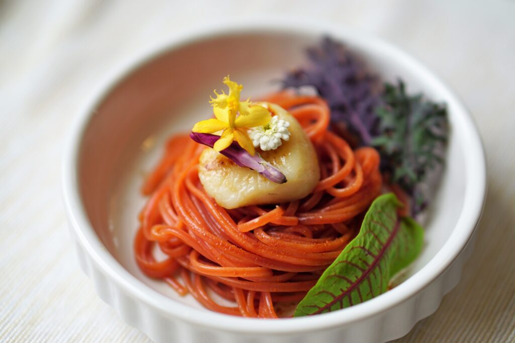 Orange pasta with scallop and edible flowers.