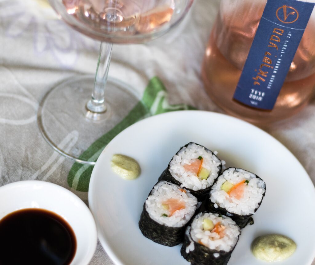 Sushi on a white plate with a rosé wine and soy sauce.