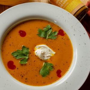 Butternut squash soup in a white bowl with garnishments of sour cream, parsley, and hot sauce.