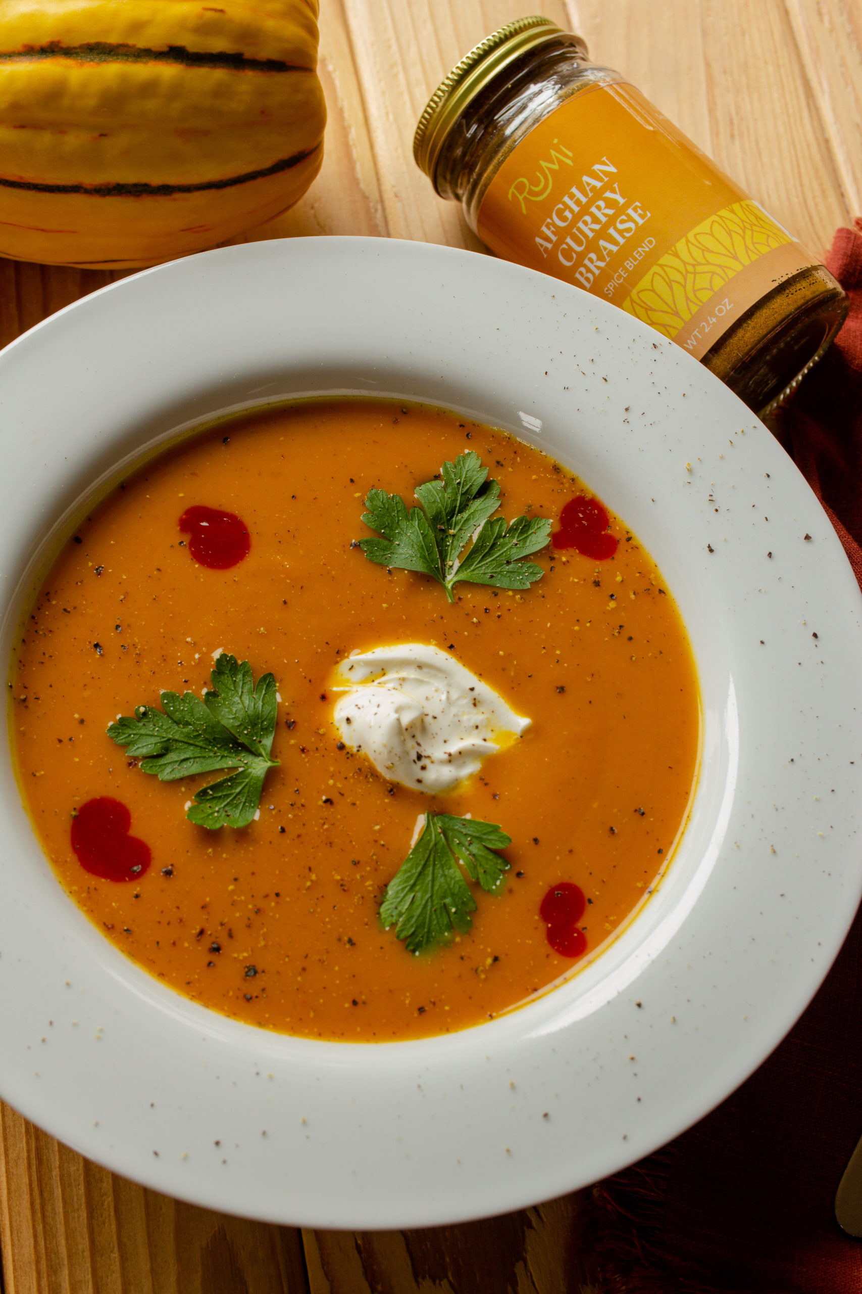 Butternut squash soup in a white bowl with garnishments of sour cream, parsley, and hot sauce.