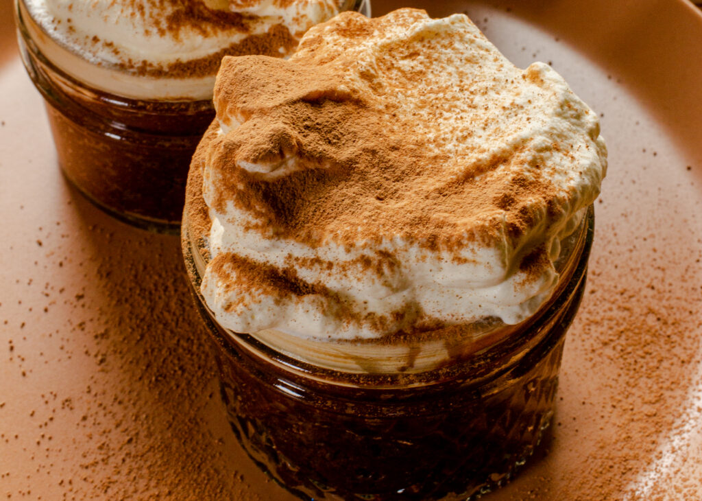 Clear ramekin filled with chocolate mousse and topped with whipped cream and cocoa powder.