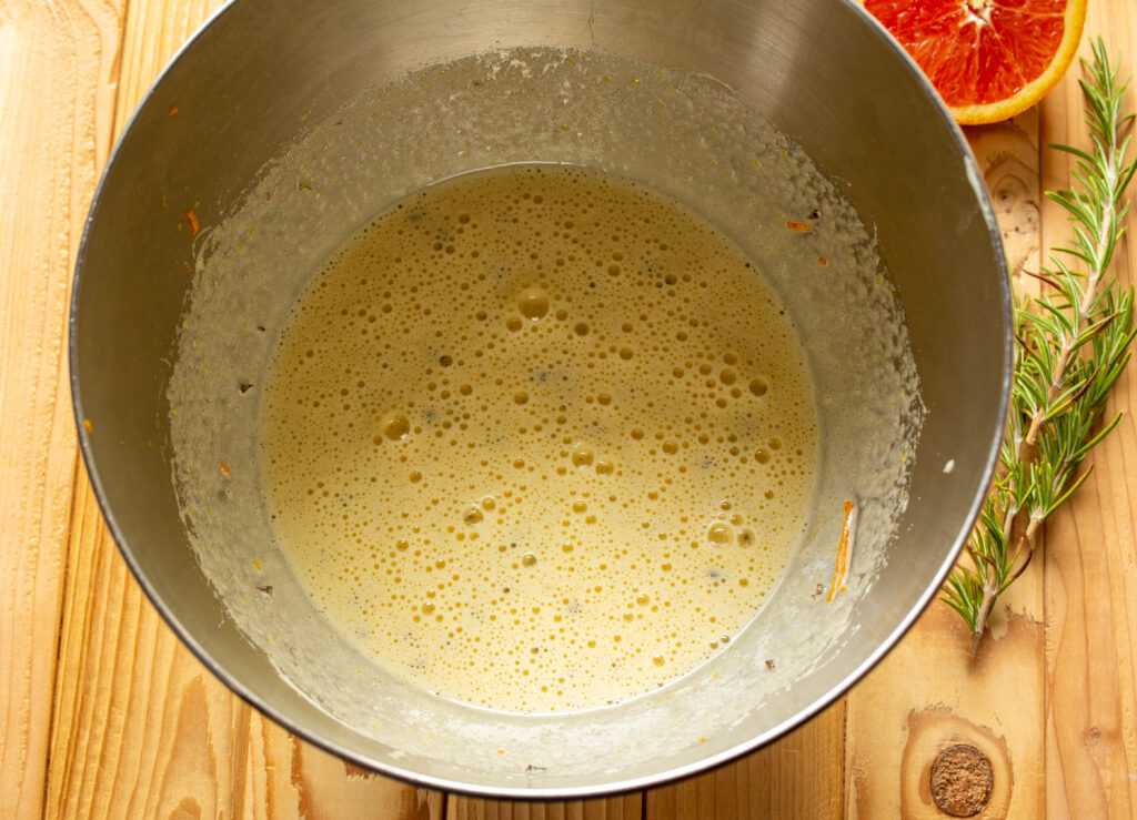 Mixer bowl filled with wet ingredients for olive oil cake that have been mixed together.