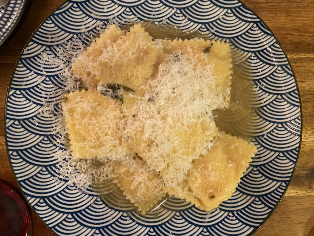 A plate of ravioli covered in cheese on a decorative blue and white plate.