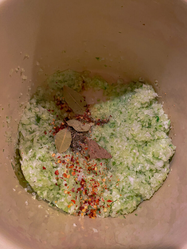Sauce pot filled with minced fennel, red chili flakes, and dried bay leaves.
