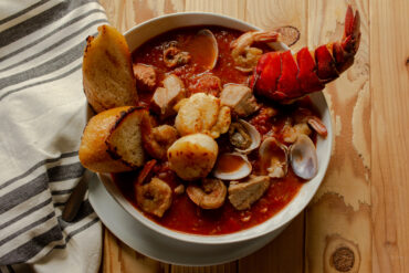 Cioppino in a white bowl with two wedges of toast in the bowl.