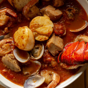 Cioppino in a white bowl with a lobster tail sticking out.