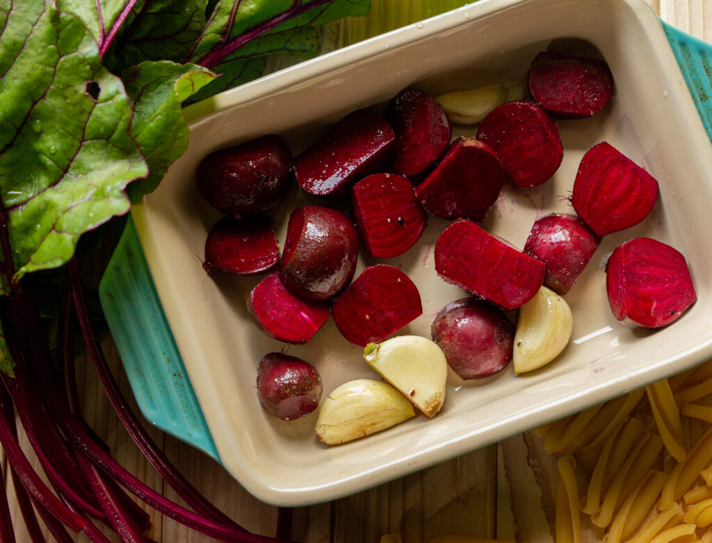 Baking dish filled with sliced beets and garlic cloves.