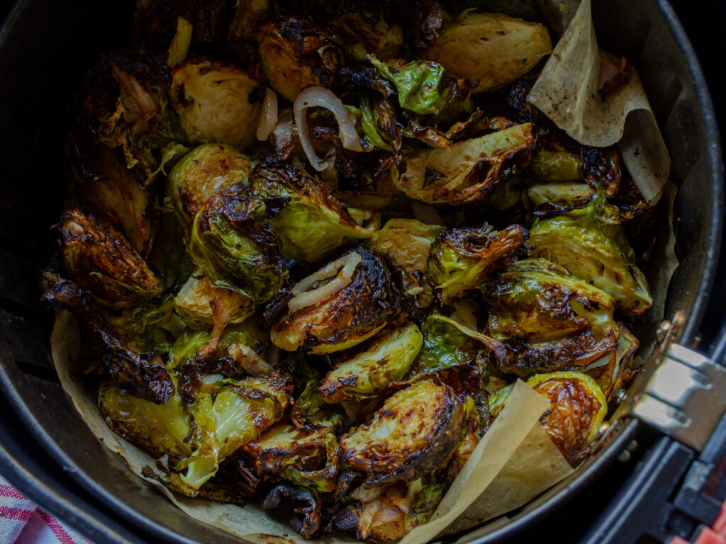 Close up of air fryer brussels sprouts with sliced shallots, in an air fryer basket with parchment paper.