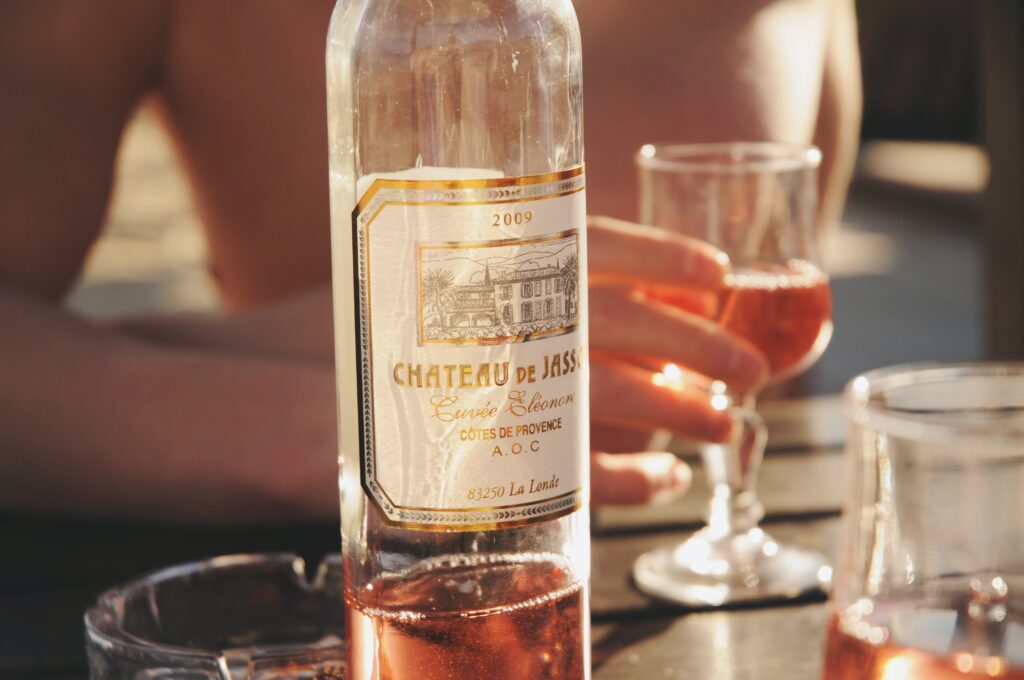 A mostly empty bottle of rosé wine with a person holding a glass of wine in the background.