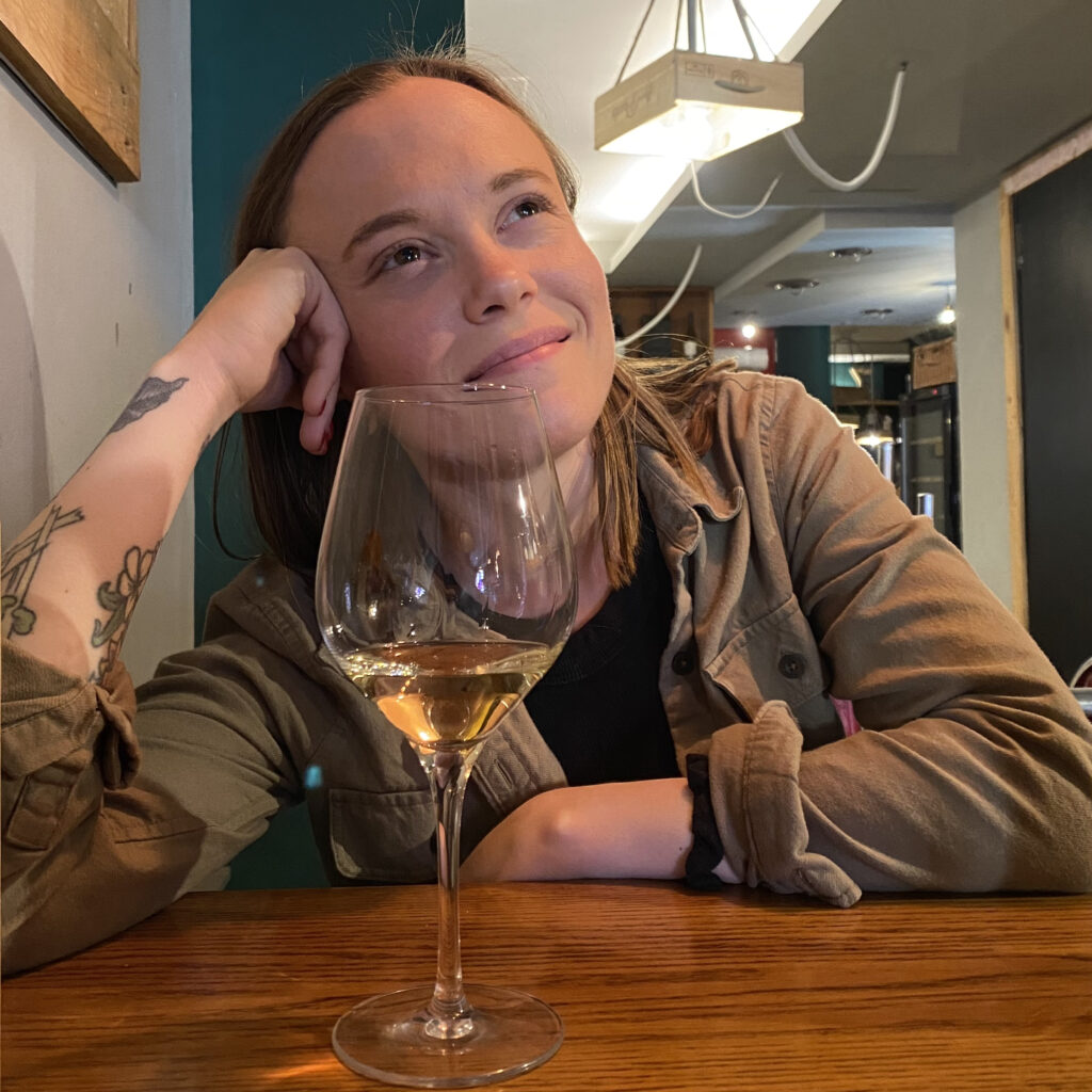 Girl looking off into the distance with a glass of wine at her table.